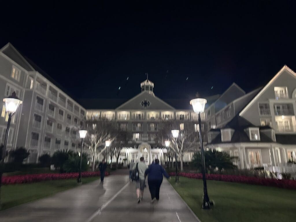 A group of people walking on the sidewalk at night.