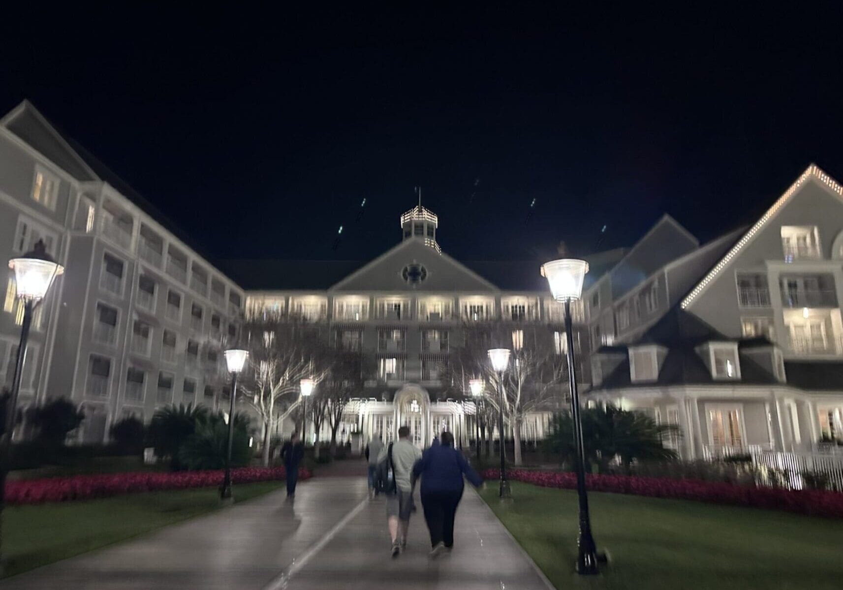 A group of people walking on the sidewalk at night.